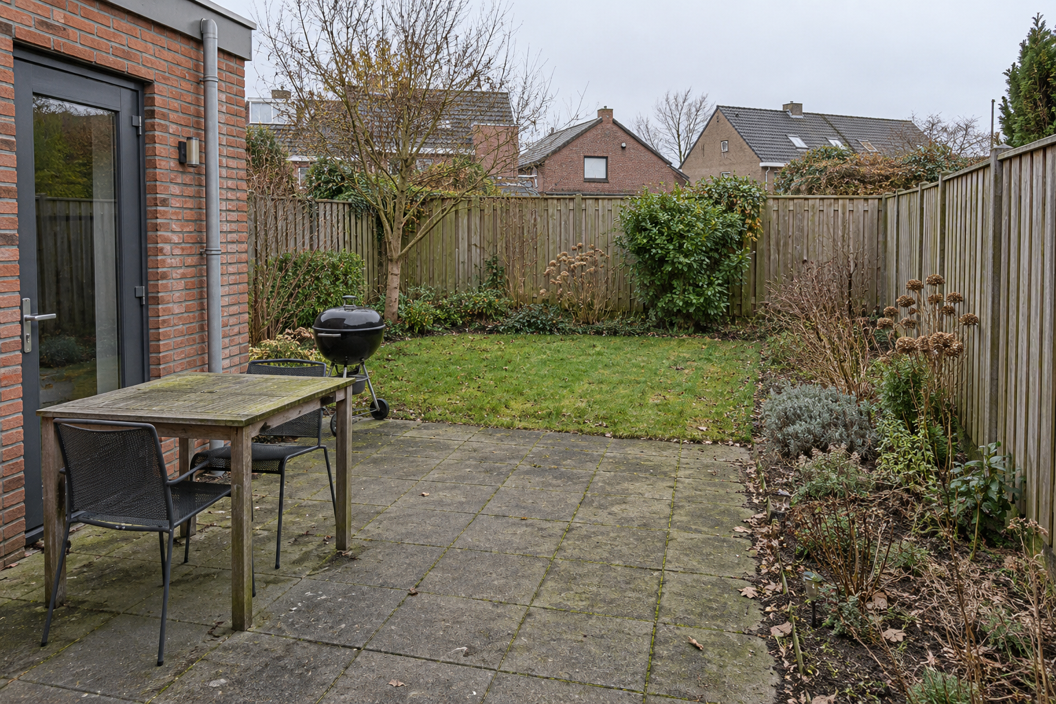 Demobeeld voor onderhoud: compacte voorjaarstuin met vervuild terras, rommelige borders, houten tafel, twee stoelen en zwarte BBQ.